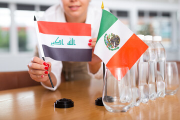 Businesswoman arranging the flags of Iraq and Mexico for a presentation and negotiations