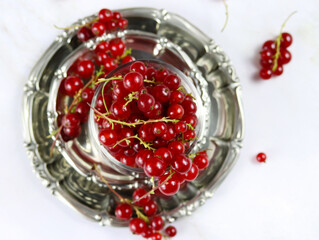 Red currant berries in metallic plate on marble table, close up, top view. Fresh red currants on light background, copy space. Atmospheric photo of ripe red currants in rustic style. Selective focus
