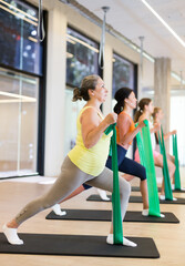 Mature elderly woman doing pilates exercise with expander tape on mat during group training at gym