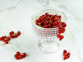 Fresh red currants in transparent glass bowl on marble table. Ripe red currant berries on light background with copy space. MInimalistic photo of red currants, selective focus