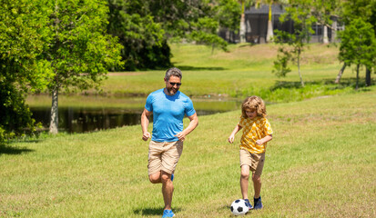 Fototapeta premium Active father son play football in summer. Father and child son teaming up outdoor. Father dad and son enjoying outdoor activities together. chasing after the ball. adventures between father and son