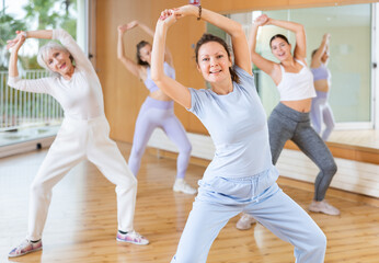 Practiced middle-aged woman engaging in aerobics in dance studio during workout session. Women...