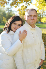 Fototapeta premium Husband and wife in white warm clothes posing for the camera in the autumn park on a sunny day
