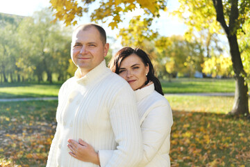 Husband and wife in white warm clothes posing for the camera in the autumn park on a sunny day
