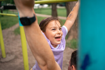 Young child daughter playing with father on the workout outdoors gym. Happy emotions. Healthy...