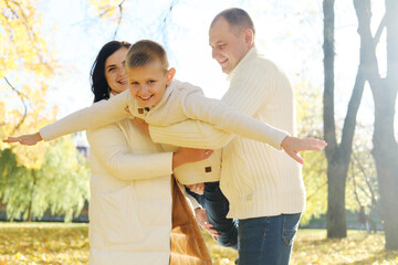 Parents hold their son like an airplane standing in the rays of autumn sun