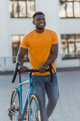 Smiling positive african amrican man standing near bicycle on street