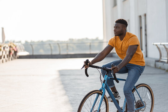 Full length view of handsome smiling African American man riding bicycle on urban street