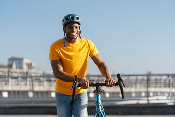 Cheerful african american man in protective helmet walking street with bicycle