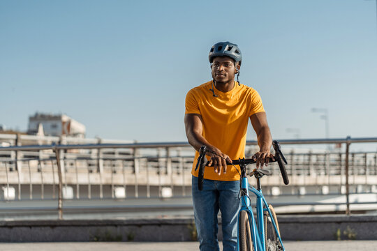 Smiling positive african amrican man wearing helmet standing near bicycle on street