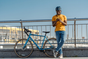 Smiling african american man in helmet holding mobile phone near bicycle