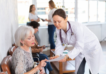 Polite qualified female doctor in white coat showing results of medical examination and explaining prescribed treatment 