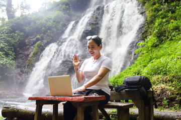 a female freelancer working in nature with a waterfall in the background.  remote working and...