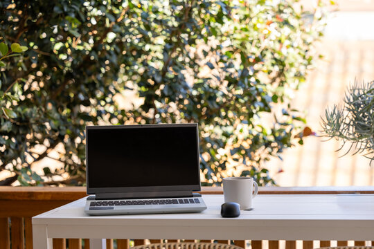 Work from home set up with laptop and mug on outdoor table with plants in background