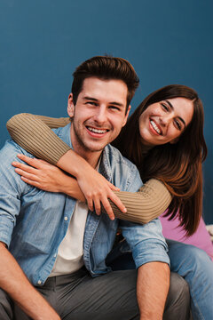 Vertical portrait of happy young couple in love, cudding and relaxing in their modern apartment. Smiling wife embracing her husband and looking at camera enjoying their new home together. Relationship