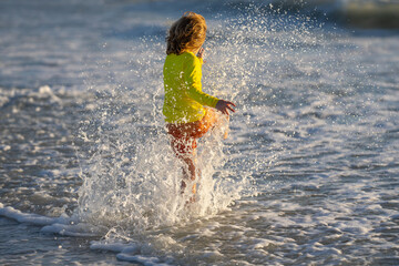 Child splashing in sea. Kid play with sea water drop. Little kid play in water and making splash. Child have fun with drops. Kid running into sea water on summer holidays. Kid boy running along ocean.