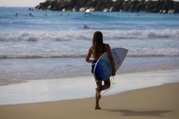a woman jogging on the beach holding her surfboard