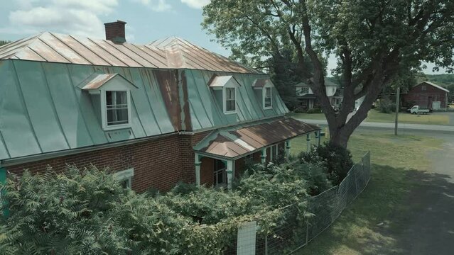 Side and down pan of an abandoned home with a tree on the side and giant bushes in the front. Oldschool old town house with a street in the back blue sky and simpson clouds