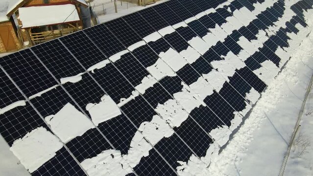 Aerial view of snow melting from covered solar photovoltaic panels at sustainable electric power plant for producing clean electrical energy. Low effectivity of renewable electricity in winter