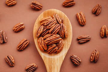 Pecan nuts close-up in a wooden spoon on a brown background.shelled pecans. Healthy fats. Keto diet...