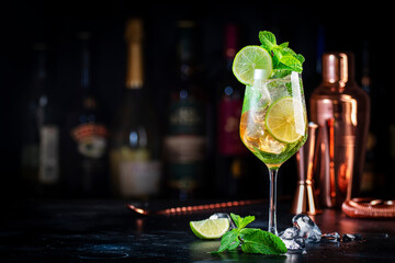 Hugo spritz alcoholic cocktail drink with dry sparkling wine or prosecco, elderflower syrup, soda, lime, mint and ice, dark bar counter background, save space
