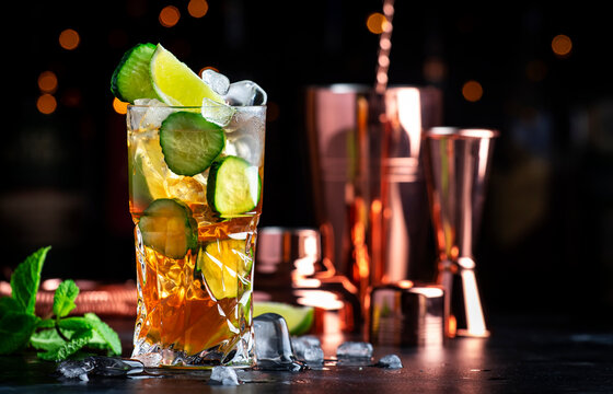 Pimms with cucumber, lime and ice - alcoholic cocktail drink with vodka, ginger beer and lemon juice, dark bar counter background, copy space.