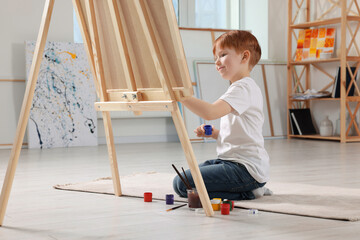 Little boy painting in studio. Using easel to hold canvas