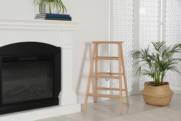 Wooden folding ladder between fireplace and potted plant in room
