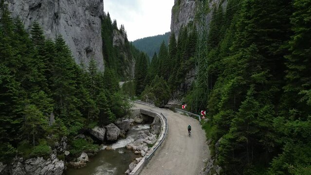 Woman cyclist riding between the mountains. Gravel biking adventure in the Bucegi Natural Park. A female cyclist, dressed in cycling kit and wearing a white helmet, is training on a gravel road.
