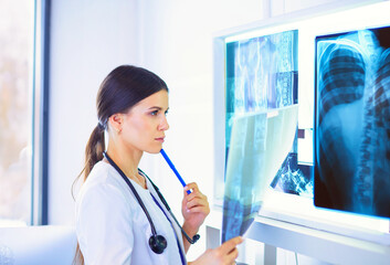Young female doctor with stethoscope examining X-ray at doctor's office