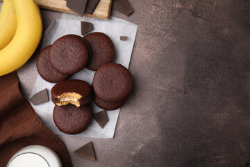 Tasty banana choco pies, pieces of chocolate and fruits on textured table, flat lay. Space for text