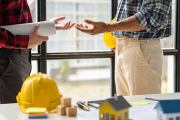 Engineer and contractor planning projects together at desk with blueprints.