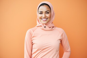 Fototapeta premium Portrait of smiling muslim woman in sportswear against orange background