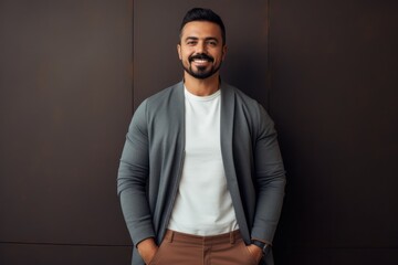 Fototapeta premium Handsome young man smiling and looking at camera while standing against brown wall