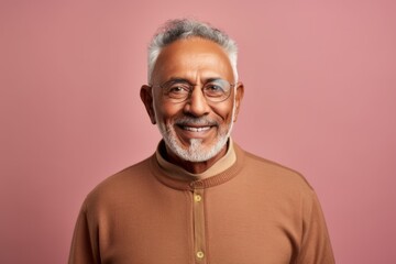 Portrait of a happy senior Indian man wearing eyeglasses smiling at the camera while standing against pink background