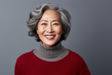 Portrait of a smiling senior asian woman in red sweater, over grey background
