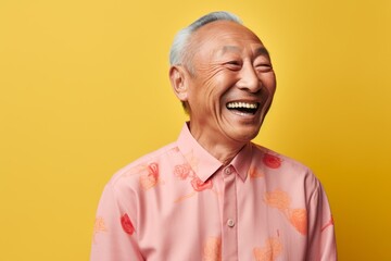 Obraz premium Portrait of a happy senior asian man laughing on yellow background