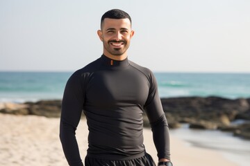 Fototapeta premium Portrait of smiling man in wetsuit standing on sandy beach