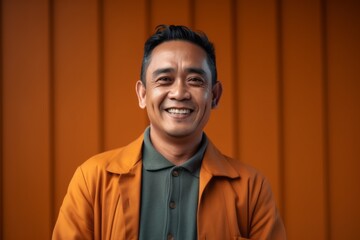 Portrait of a smiling asian man in yellow coat against orange background
