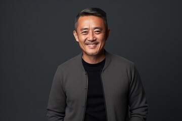 Fototapeta premium Portrait of smiling mature asian man in black sweater on grey background