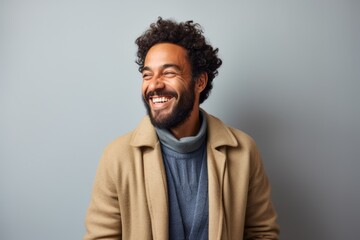 happy african american man in beige coat laughing on grey background