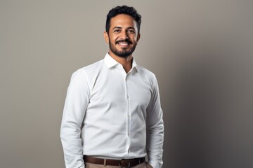 Obraz premium Portrait of a handsome indian man smiling at camera while standing against grey background