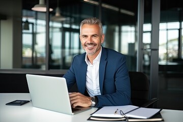 Fototapeta premium Smiling mature adult business man executive sitting at desk using laptop. Happy busy professional mid aged businessman ceo manager working on computer corporate technology in office