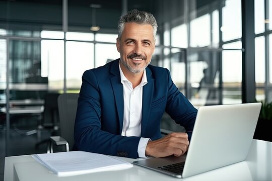 Smiling mature adult business man executive sitting at desk using laptop. Happy busy professional mid aged businessman ceo manager working on computer corporate technology in office