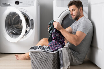 Man with clothes near washing machine. Laundry cleaning. Housework, homework, male housekeeper. Husband man doing laundry at home. Washer and dryer at home.