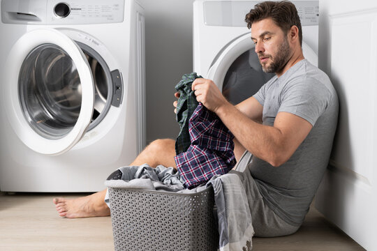 Man with clothes near washing machine. Laundry cleaning. Housework, homework, male housekeeper. Husband man doing laundry at home. Washer and dryer at home.