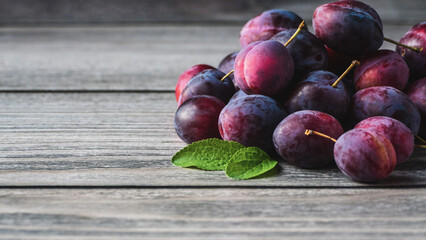 Plums on wooden table, harvested prune fruits green leaves in a pile closeup, copy space