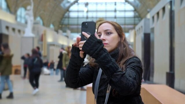 Thoughtful Latina woman tourist with smartphone looking up and enjoying view in Orsay Museum in Paris, France while relaxing on weekend