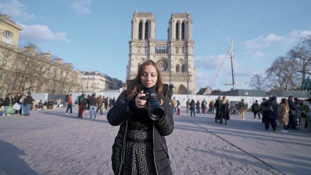 Positive Latina woman tourist smiling and taking photos with professional photo camera while standing against landmark of Paris, France in Notre Dame cathedral