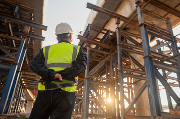 Engineer architect in safety clothes and helmet working on tollway construction site Engineer supervises road construction, commands with Walkie-Talkie radio communications.